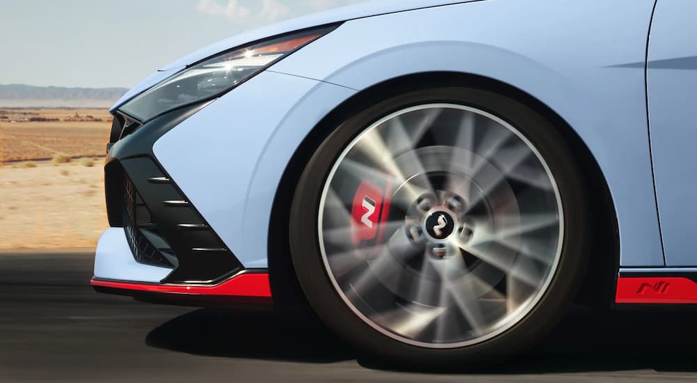 A close-up of the front bumper and driver's side wheel on a light blue 2024 Hyundai Elantra N.