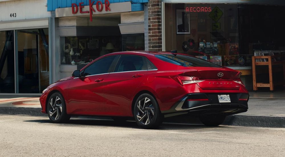 Rear angle view of a red 2024 Hyundai Elantra Limited parked by a city curb.