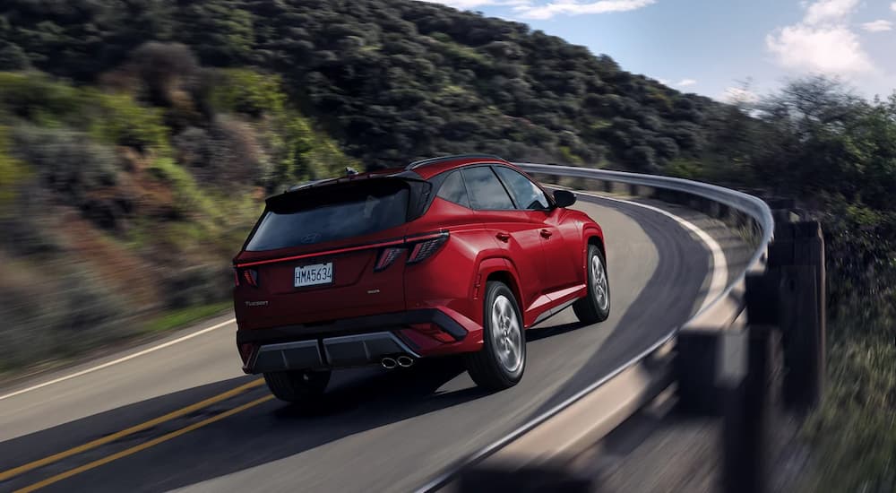A rear view of a red 2025 Hyundai Tucson Hybrid Ultimate driving up a steep mountain highway.