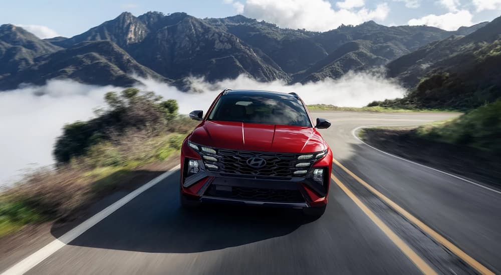 A red 2025 Hyundai Tucson Hybrid Ultimate is driving on a mountain road.