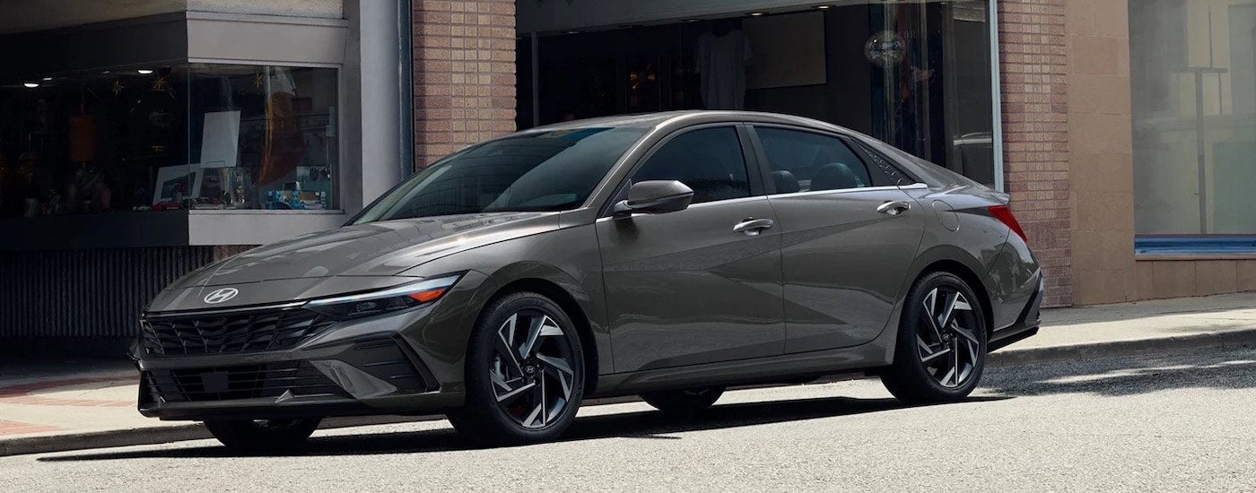 A grey 2024 Hyundai Elantra Hybrid is shown from the side while parked on a city street.