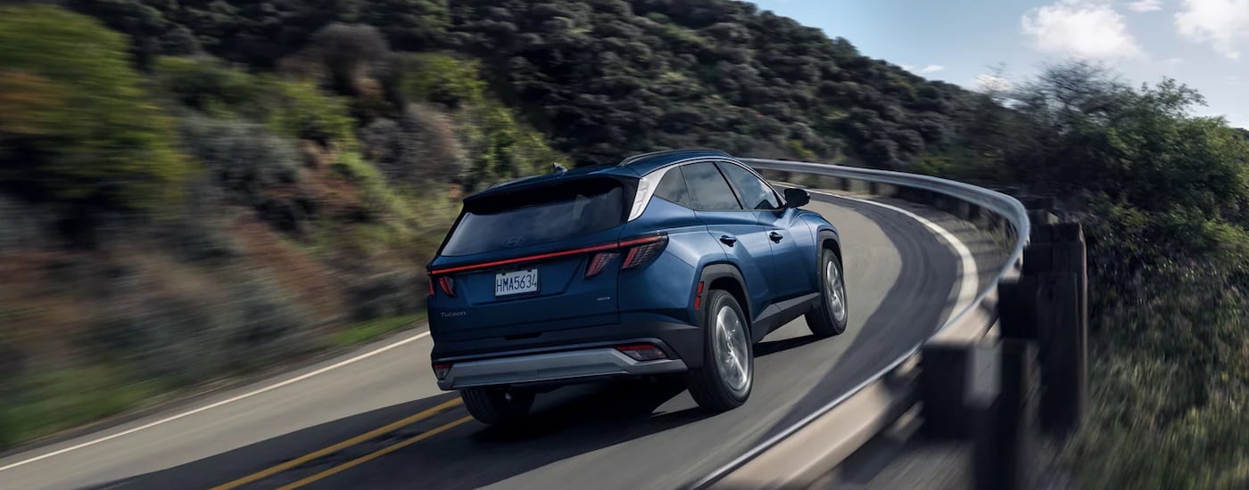 Rear of a dark blue 2026 Hyundai Tucson driving up a hill.