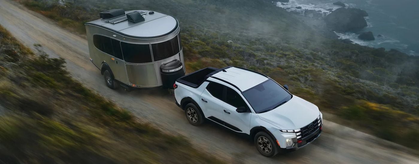White 2026 Hyundai Santa Cruz towing a camper along the coast.