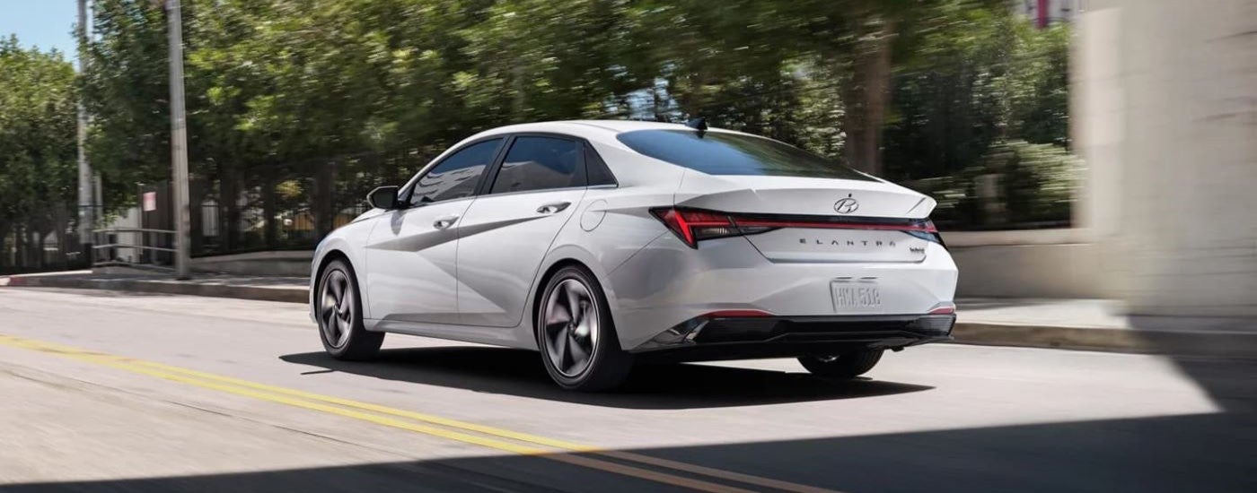 A white 2021 Hyundai Elantra Hybrid is shown from behind driving on a city street.